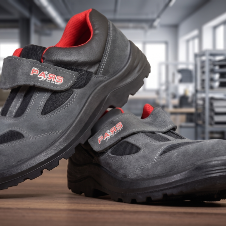 Close-up of gray safety sneakers with red inner lining resting on a wooden table in a busy workshop/studio.